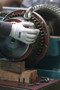 A gloved hand adjusts a gear in industrial machinery, focusing on precision.