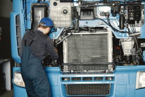 Mechanic in uniform working on a truck engine in an industrial workshop. Perfect for automotive maintenance themes.