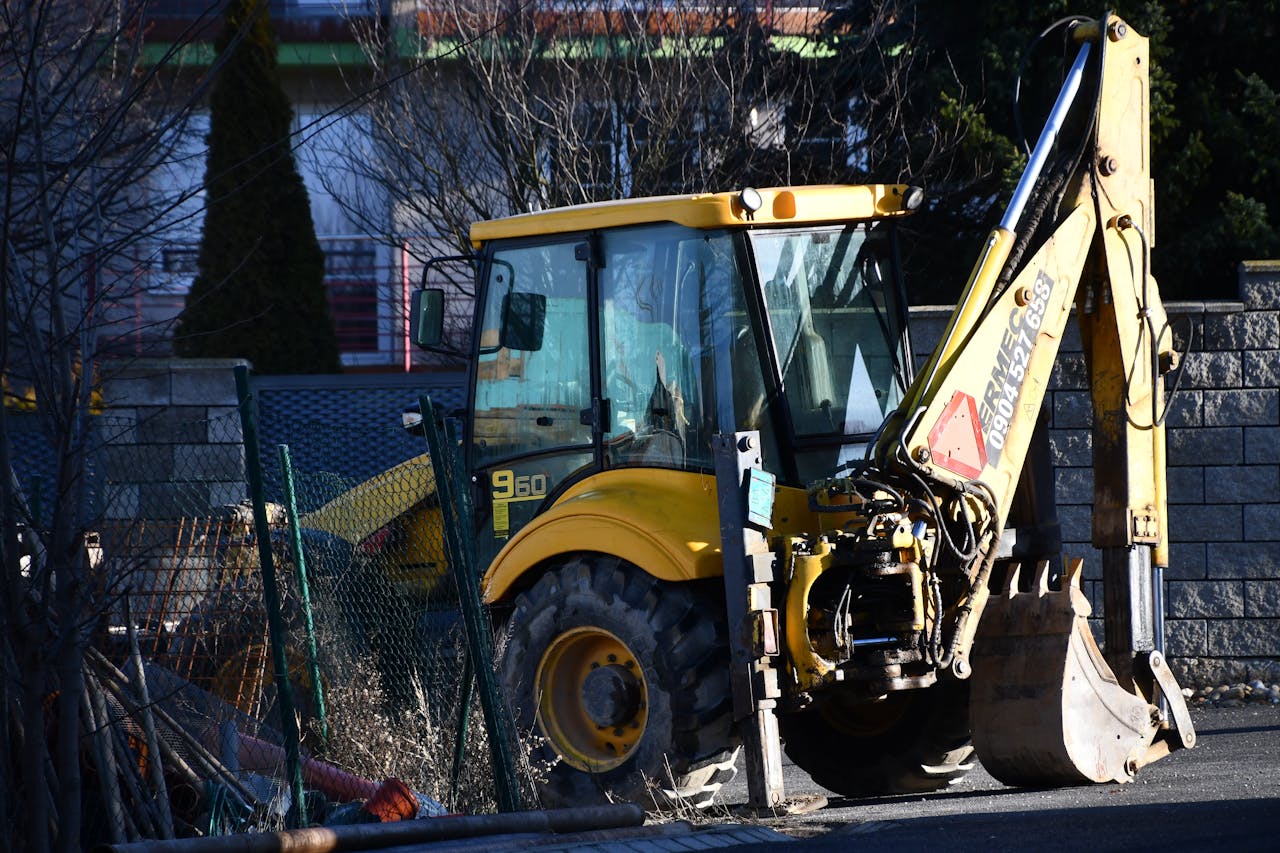 A yellow excavator rests on an urban construction site during daylight.