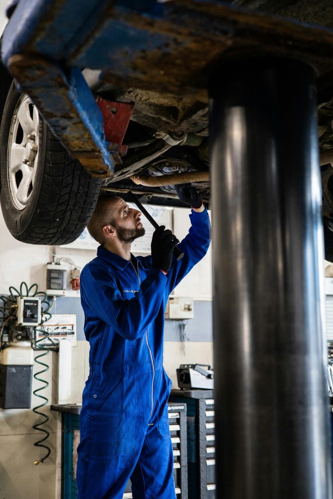 pexels photo 8986068 8986068 Mechanic in blue coveralls inspecting car undercarriage on hydraulic lift.